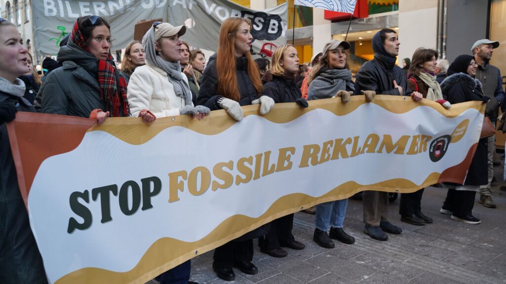 Aktivister står med et "Stop Fossile Reklamer"-banner ved Folkets Klimamarch i november 2025